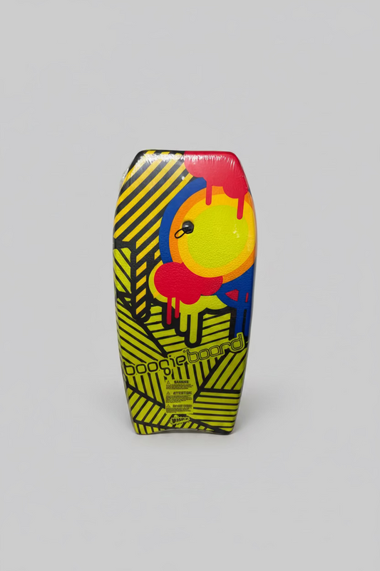 A brightly colored bodyboard standing upright against a white cardboard box. The board features a bold yellow and black striped base with a large central graphic in red, yellow, blue, and orange, and the words 'boogieboard' printed near the bottom.